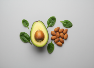 Minimalistyczna kompozycja produktów wspierających dietę ketogeniczną: awokado, migdały i szpinak na jasnym tle.